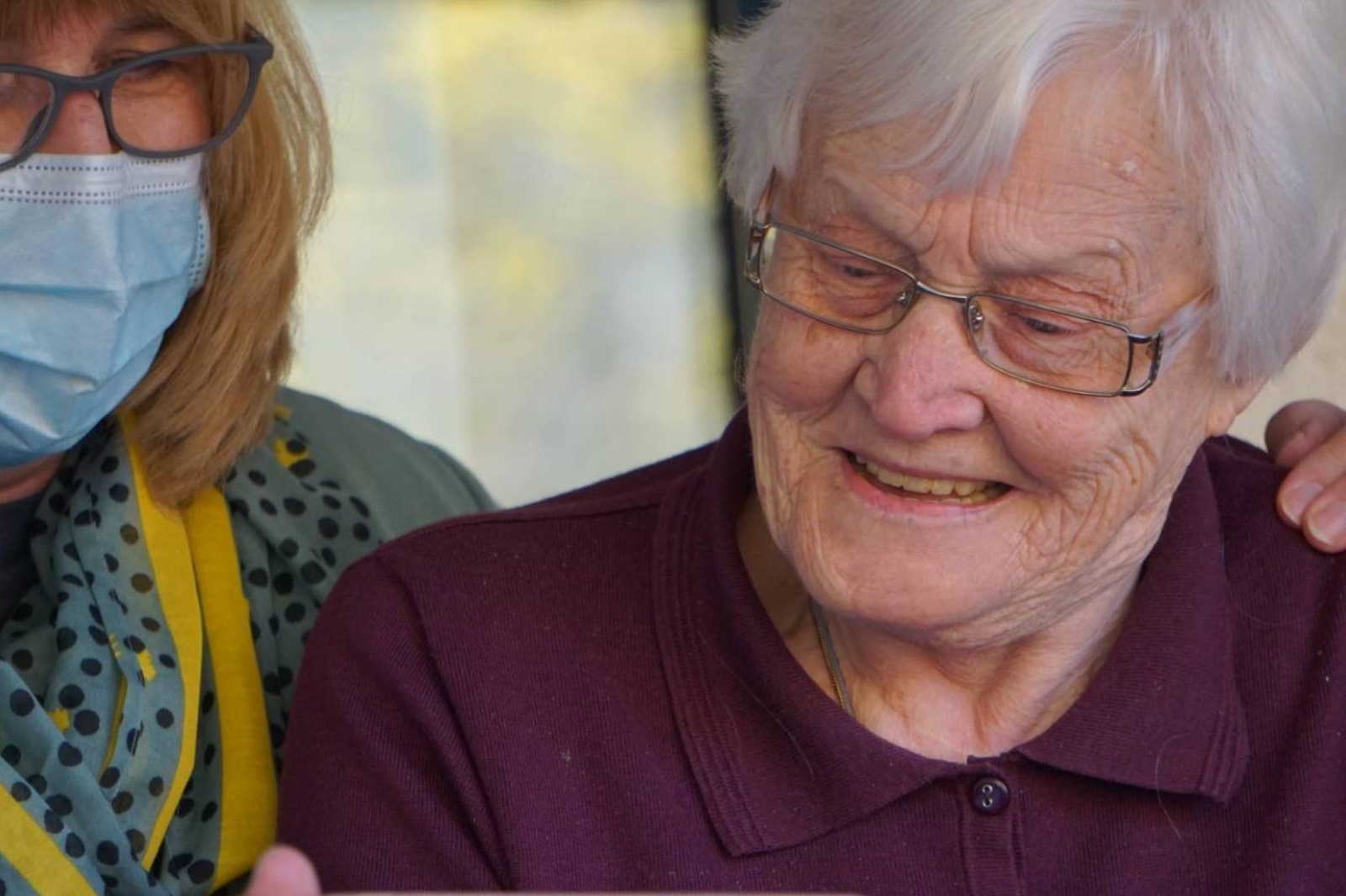 Una donna con la mascherina mostra uno smartphone a una donna anziana