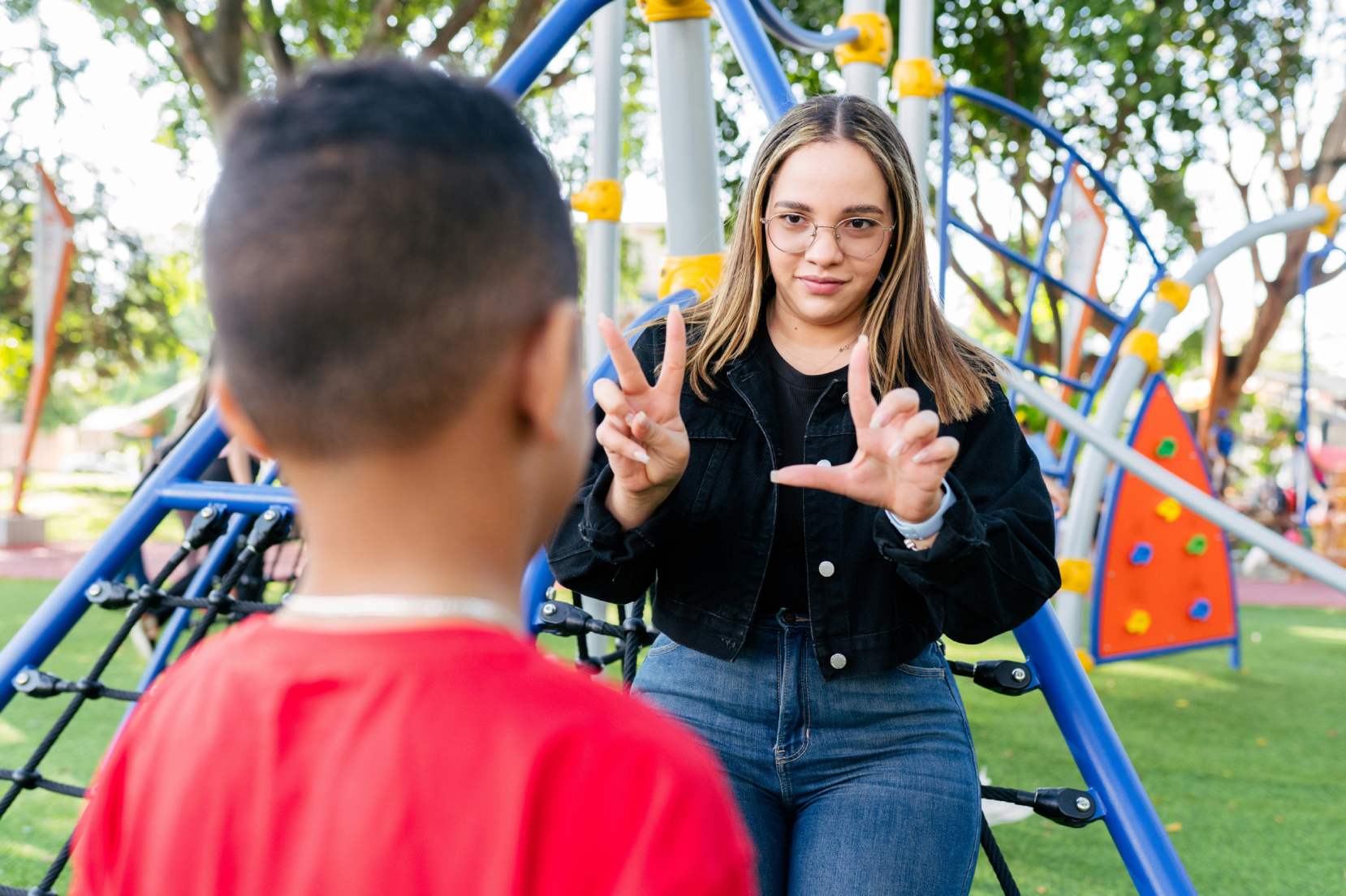 Bambino di spalle con maglietta rossa che parla in LIS con un'operatrice